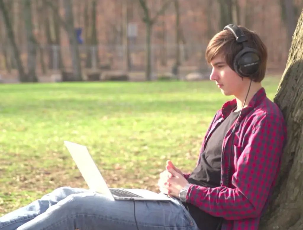 Marvin Alberg, Gründer von Neowake® sitzt in einem grünen Park mit einem Laptop auf dem Schoß und Kopfhörern auf dem Kopf.
